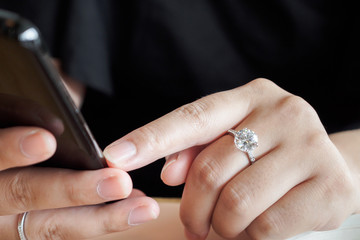 Woman with diamond ring on hand using smartphone in cafe restaurant