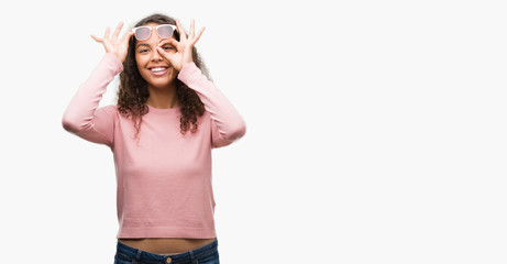Obraz na płótnie Canvas Beautiful young hispanic woman wearing sunglasses doing ok gesture with hand smiling, eye looking through fingers with happy face.