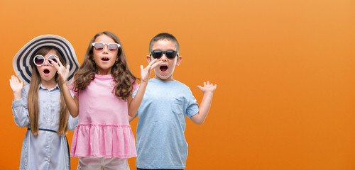 Group of boy and girls kids over orange background very happy and excited, winner expression celebrating victory screaming with big smile and raised hands