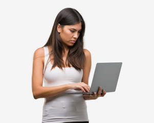 Naklejka premium Young hispanic woman using computer laptop with a confident expression on smart face thinking serious