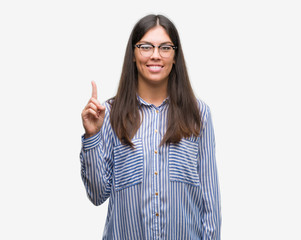 Young beautiful hispanic business woman showing and pointing up with finger number one while...