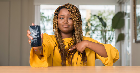 African american woman showing broken smartphone with surprise face pointing finger to himself