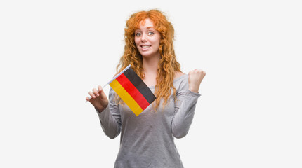 Young redhead woman holding flag of Germany screaming proud and celebrating victory and success very excited, cheering emotion