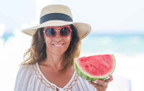 Middle Age Brunette Woman By The Sea Eating Watermelon With A Happy Face Standing And Smiling With A Confident Smile Showing Teeth