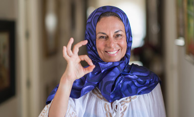 Middle age brunette arabian woman wearing colorful hijab doing ok sign with fingers, excellent symbol