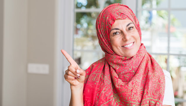 Middle aged muslim woman wearing hijab very happy pointing with hand and finger to the side