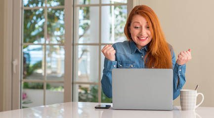 Redhead woman using computer laptop at home screaming proud and celebrating victory and success...