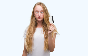 Fototapeta premium Blonde teenager woman holding credit card with a confident expression on smart face thinking serious