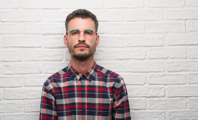 Young adult man standing over white brick wall with a confident expression on smart face thinking serious