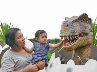 Asian baby girl, together with her aunt, enjoy looking and touching a dinosaur - an excursion with...