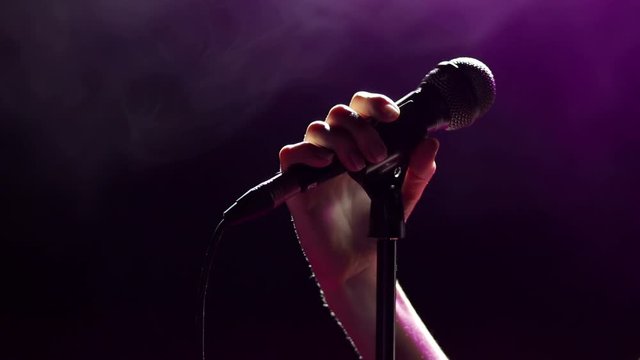Close-up of a singer's hand on a microphone in the dark on a black background. Female singer on the stage holding a microphone.