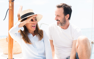 Obraz premium Middle age couple traveling on sailboat with happy face smiling doing ok sign with hand on eye looking through fingers