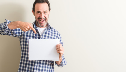 Senior man holding blank paper sheet very happy pointing with hand and finger