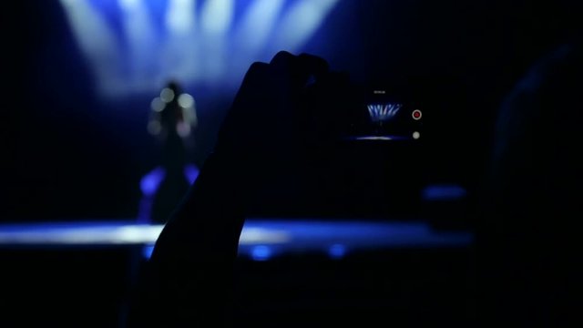 People records a video from a concert of a beautiful singer on a smartphone.