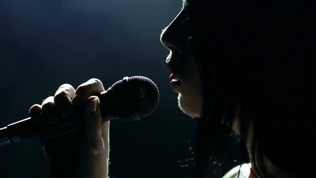 Portrait of a beautiful singer with long hair on a dark smoky stage in the spotlight. Female singer on the stage holding a microphone.