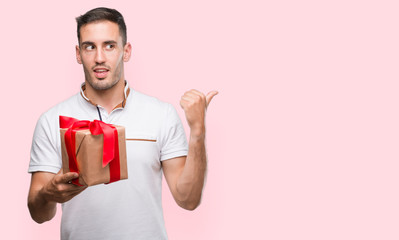 Handsome young man giving a present pointing with hand and finger up with happy face smiling