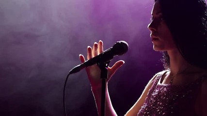 Close-up of the face of the singer with microphone on a black smoky background. The singer sings a song on stage in the dark, smoke, purple light, concert. - Powered by Adobe