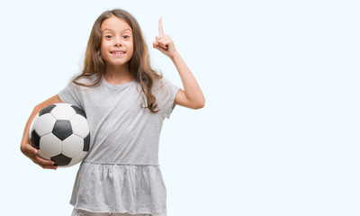 Brunette hispanic girl holding soccer football ball surprised with an idea or question pointing...
