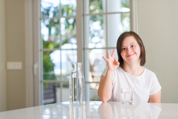 Down syndrome woman at home drinking water doing ok sign with fingers, excellent symbol