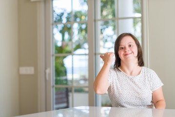 Down syndrome woman at home pointing and showing with thumb up to the side with happy face smiling