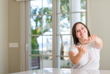 Down syndrome woman at home approving doing positive gesture with hand, thumbs up smiling and happy for success. Looking at the camera, winner gesture.
