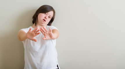 Down syndrome woman standing over wall afraid and terrified with fear expression stop gesture with...