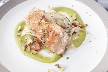 Grilled salmon steak served with green pesto sauce on top with pistachio