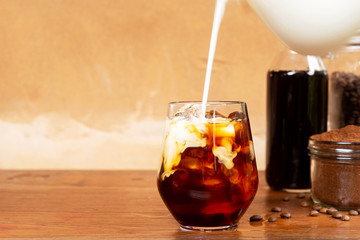 Pouring milk into a glass of homemade cold brew coffee on wooden table