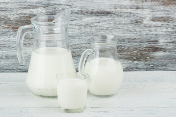Milk in the glass jugs on the wooden background