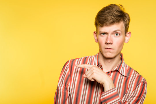 Look There. Funny Comic Man Pointing Sideways With A Hand. Portrait Of A Young Guy On Yellow Background. Free Space For Advertisement.