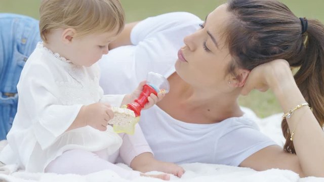 Young mother and daughter relaxing in a park and playing with baby toys