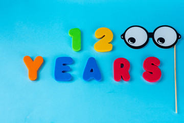 12 years old celebrating classic logo, Masquerade Masks on Stick. Colored happy anniversary 12 th  numbers on blue background. Greetings celebrates card. Traditional digits of ages. Flat lay.