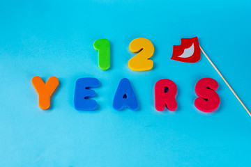 12 years old celebrating classic logo.Cute Masquerade Masks lips on Stick. Colored happy anniversary 12 th  numbers on blue background. Greetings celebrates card.Traditional digits of ages. Flat lay.