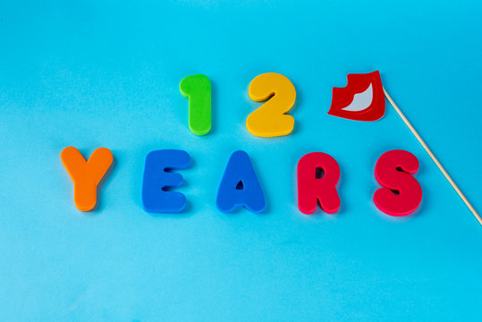 12 years old celebrating classic logo.Cute Masquerade Masks lips on Stick. Colored happy anniversary 12 th  numbers on blue background. Greetings celebrates card.Traditional digits of ages. Flat lay.