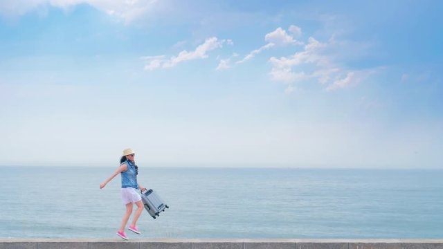 Happy woman walking along the embankment with suitcase on the sea background