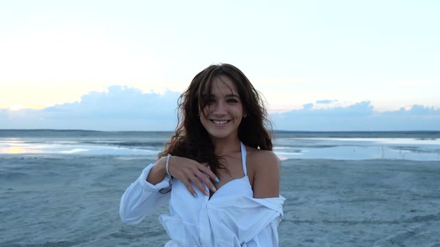 Cheerful girl turns in front of the camera on a wild beach at sunset