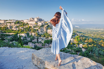 Provence, France. Young French lady dressing traditional Provencal apparel, enjoying the sunset at Gordes, Provence with incredible landscape panorama of valley and ancient hill top town Gordes.