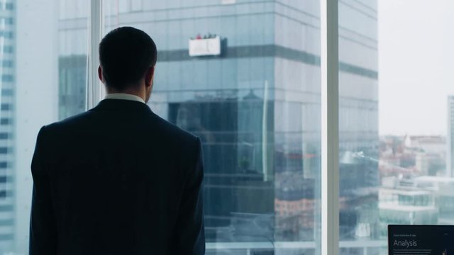 Following Shot of the Confident Businessman in a Suit Walking Through His Office and Looking out of the Window Thoughtfully. Stylish Modern Business Office with Personal Computer and Big City View.