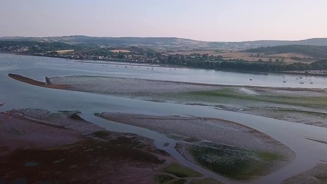 Sky view of the thriving coastal town of Lympstone England. Boats are docked close to shore, the homes an businesses are seeing in the distance, and the hills are in the background.