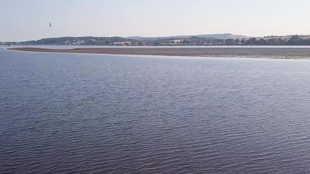 Aerial footage of the the ocean off of the shores of Lympstone, a historical town in southwest England. In midst the ripples a buoy is floating in the water.