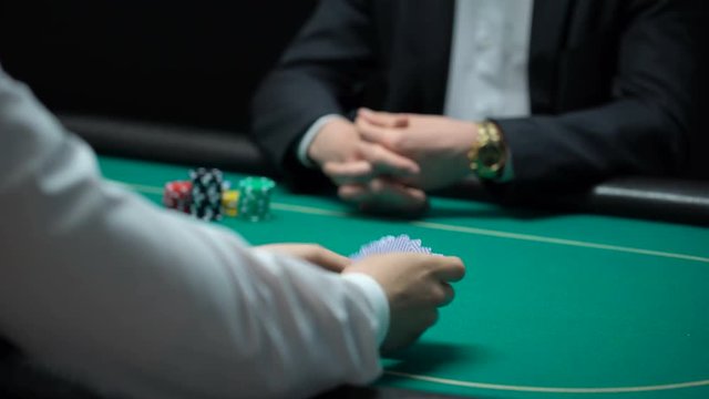 Male croupier shuffling and dealing cards at casino, player checking combination
