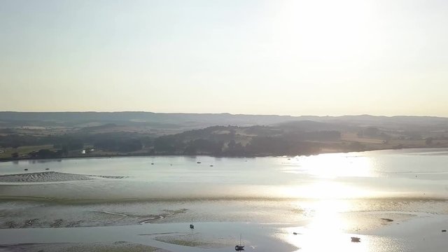 Aerial view of land and docked boats off of the shores of Lympstone England. The sun is high in the sky and its rays are reflecting in the water.