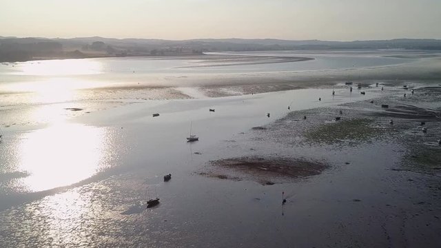 Flying over docked sail boats and ships in the evening glow making them silhouettes. The boats are close to the beach of Lympstone England.