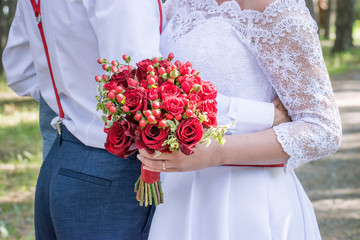 Beautiful bouquet of a bride with red roses close-up on a walk of the newlyweds in the park