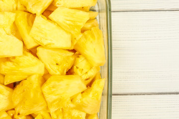 Tabletop view - close up of ripe pineapple cut into pieces, in glass bowl placed on white boards desk.