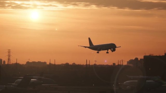 Silhouette of a commercial airplane landing on an airport at a beautiful golden sunset. Slow motion