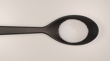 TOP VIEW: White salt in a plastic spoon on a table