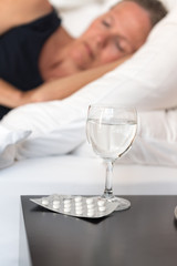 Frau im Bett mit einem Glas Wasser und Schlaftabletten davor