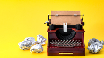 Creative writing, vintage technology and artistic pursuit concept with an retro typewriter surrounded by crumpled paper balls isolated on minimalist bright yellow background with copy space