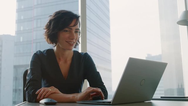 Successful Businesswoman Working on a Laptop in Her Modern Office. Stylish Beautiful Woman Doing Important Job. In the Window Big City Business District View. 